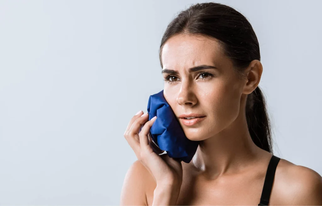 A person holding an ice pack to their cheek, managing swelling after a tooth extraction.