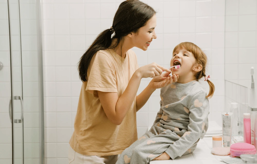 A mother helping her daughter to brush her teeth